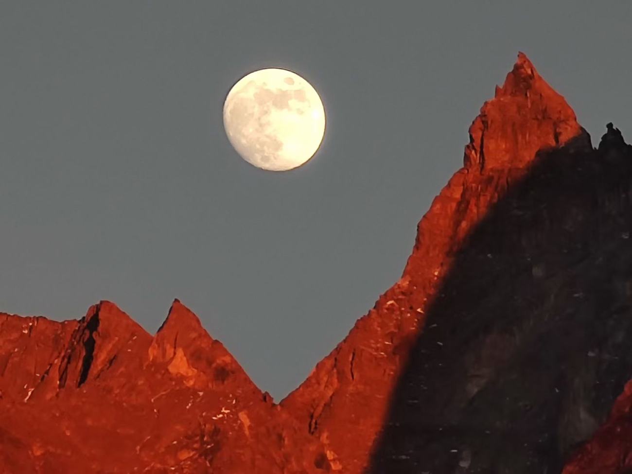 Full moon rising between red sunlit peaks