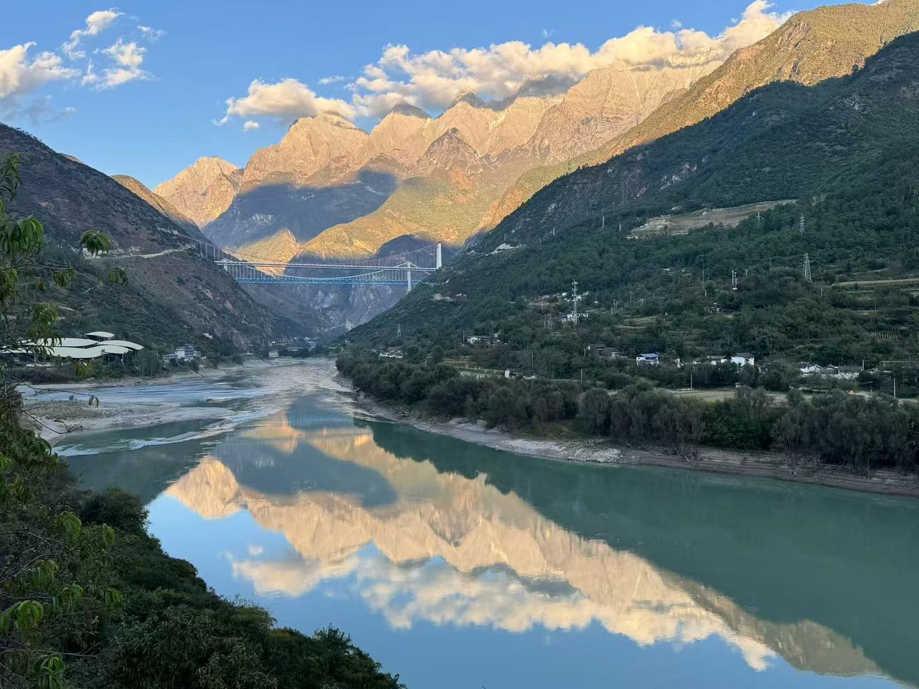 The Jade Dragon range lit gold at sunset and reflected in a still stretch of the river, with two bridges far down the valley