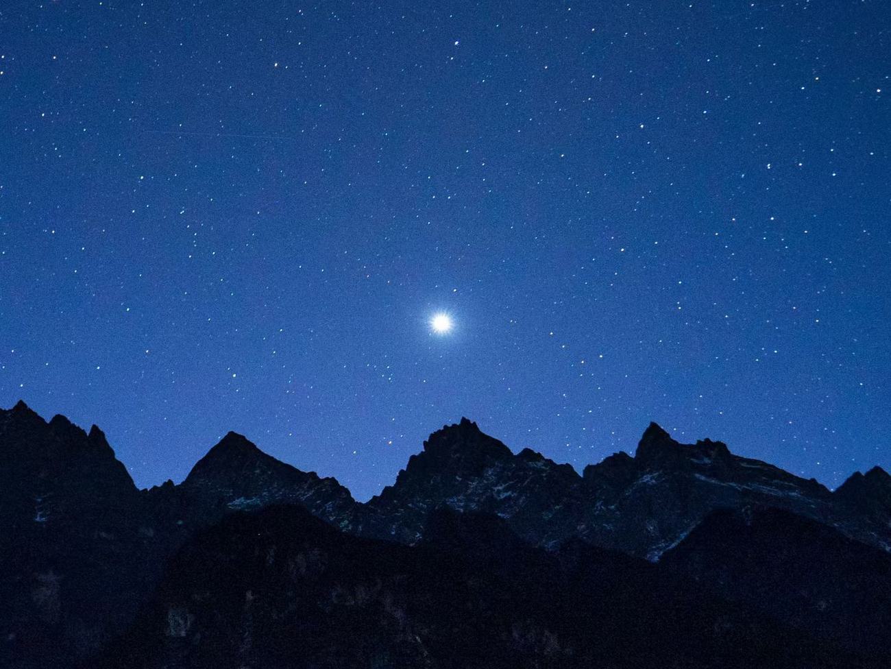 A bright star over dark mountain silhouettes in a night sky full of stars