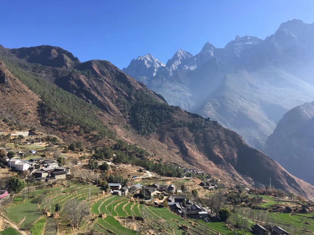 A village with terraced fields on the slope and the Jade Dragon range in the haze