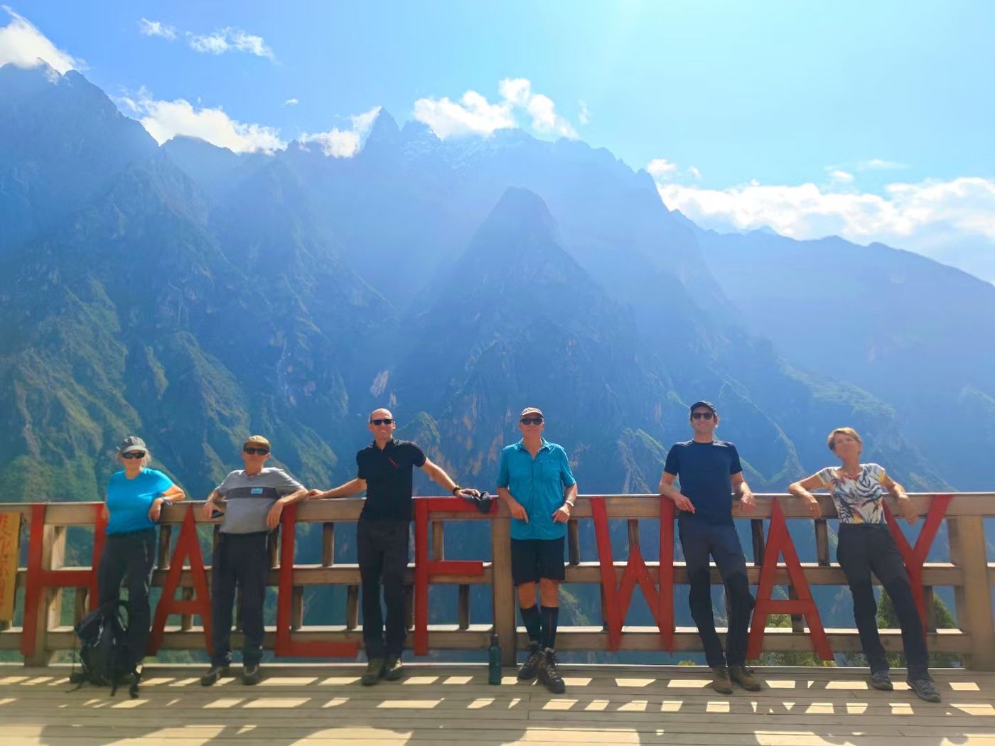 Six hikers leaning on the red lettered HALFWAY railing, with the gorge wall rising behind them