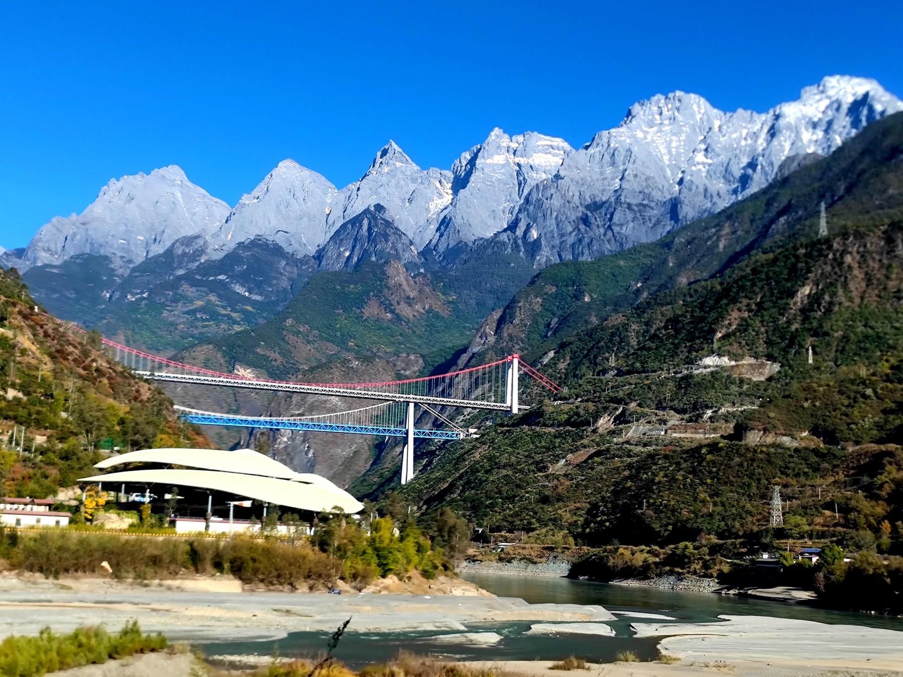 Snow-covered peaks of Jade Dragon Snow Mountain above the Jinsha River and two suspension bridges under a deep blue sky